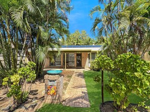 Una casa con fachada de ladrillo, un pequeño patio con jacuzzi y exuberante vegetación tropical.