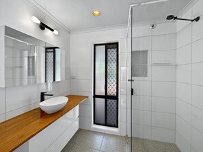 Un baño moderno con un lavamanos blanco, encimera de madera y cabina de ducha de vidrio.