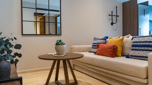 Uma sala de estar moderna com um sofá, uma pequena mesa redonda, um vaso decorativo e um luminário fixado na parede.