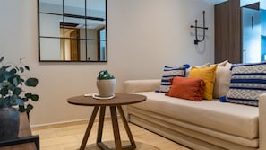 A modern living room with a sofa, a small round table, a decorative vase, and a wall-mounted light fixture. - Paraíso Swim up Selva Ubicación Top (Tulum)