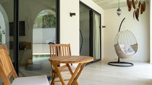 A wooden chair and table on a balcony with a hanging chair, glass doors, and a view of a scooter. - Paraíso Swim up Selva Ubicación Top (Tulum)