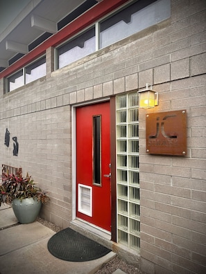 Ein Gebäude mit roter Tür, einem Metallschild mit 'JK Studios' und einem Blumentopf neben dem Eingang.