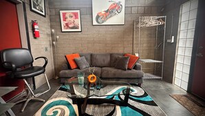 A room with a gray sofa, a black chair, a glass coffee table, a patterned rug, a motorcycle painting, and a fire extinguisher. - Mid Century Modern Casita, kitchenette, laundry, AC & pool in Uptown Phoenix (Phoenix)