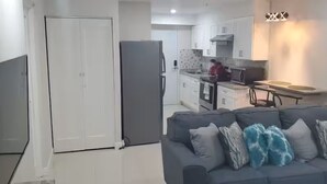 A living room with a grey sofa, a flat-screen TV, and a kitchen in the background. - Studio with private deck (Portmore)