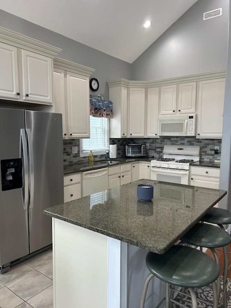A kitchen with white cabinets, a stainless steel refrigerator, a microwave, a stove, and a granite countertop.