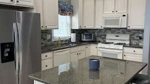 A kitchen with white cabinets, a stainless steel refrigerator, a microwave, a stove, and a granite countertop. - Family Beach Getaway – Walk to Beach, Boardwalk & Enjoy Coastal Comfort (Ocean City)