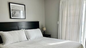 A neatly made bed with a headboard, a bedside lamp, and a framed picture on the wall. - Family Beach Getaway – Walk to Beach, Boardwalk & Enjoy Coastal Comfort (Ocean City)