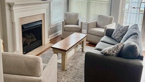 A living room with a fireplace, a television, and two windows with curtains. - Family Beach Getaway – Walk to Beach, Boardwalk & Enjoy Coastal Comfort (Ocean City)