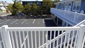 A parking lot with marked spaces, a building with a white fence, and a blue building in the background. - Bright & Welcoming 2BR Near Beach, Boardwalk & Local Attractions (Ocean City)
