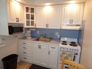 A compact kitchen with white cabinets, a microwave, a coffee maker, a stove, and a trash bin. - Bright & Welcoming 2BR Near Beach, Boardwalk & Local Attractions (Ocean City)