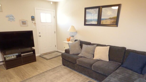 A living room with a sofa, a flat-screen TV, a lamp, and a door. - Bright & Welcoming 2BR Near Beach, Boardwalk & Local Attractions (Ocean City)