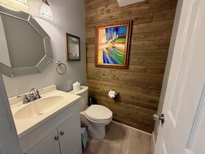 Ein Badezimmer mit Holzwand, Waschbecken, Toilette, einem gerahmten Bild und einem Spiegel.