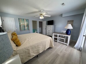 Ein Schlafzimmer mit Bett, Schreibtisch, Deckenventilator, Fernseher und einem Bild an der Wand.