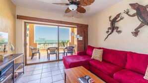 A room with a red sofa, a wooden coffee table, a ceiling fan, and a view of the beach. - Ocean View 2BR Condo at Princesa de Peñasco – Beautiful Balcony view C403 (Puerto Peñasco)