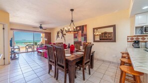 A dining area with a view of the sea, a ceiling fan, and a kitchen with a microwave. - Ocean View 2BR Condo at Princesa de Peñasco – Beautiful Balcony view C403 (Puerto Peñasco)