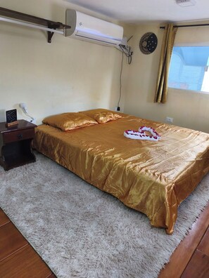 A hotel room with a bed, a bedside table, an air conditioning unit, a wall clock, and a window with curtains. - Cozy Chalet, Your Beach Retreat (Cabo de Santo Agostinho)