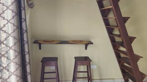 Een kamer met een houten plafond, een raam, twee krukken en een houten ladder.