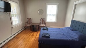 A bedroom with a bed, two chairs, a round mirror, and a television. - Charming 2-bedroom apartment in charming Attleboro (Attleboro)