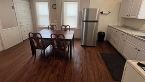 A kitchen with a stainless steel refrigerator, wooden dining table, and chairs, white cabinets, and a window with blinds. - Charming 2-bedroom apartment in charming Attleboro (Attleboro)