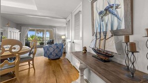 Una habitación con una mesa de comedor de madera, sillas, un reposapiés estampado, un modelo de barco en una consola y un cuadro con la imagen de un caballito de mar.