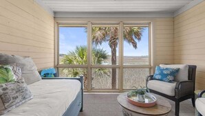 Habitación con cama, una silla, una mesita y un ventanal con vistas a palmeras.