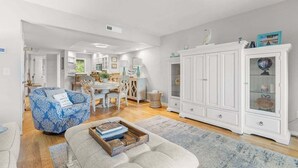 Un salón espacioso con un sofá azul estampado, un aparador blanco con puertas de cristal y un área de comedor al fondo.