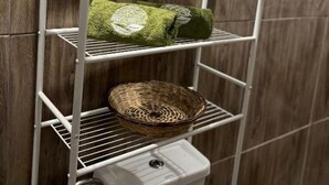 Une étagère en métal blanc, dotée de paniers, et un récipient blanc, le tout placé contre un mur en bois.