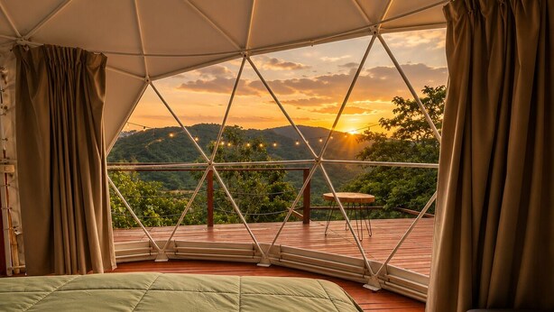 Une pièce aménagée avec une tente, un lit, un banc et une vue sur un coucher de soleil se déclinant sur un paysage montagneux.
