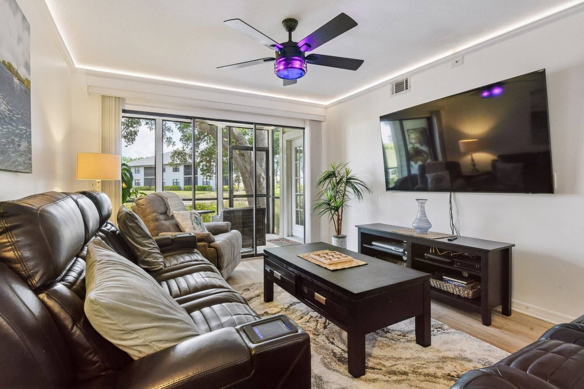 A living room with a leather sofa, a coffee table, a TV, and a ceiling fan.