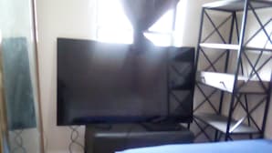 Une chambre à coucher avec un lit, une télévision, une étagère et une fenêtre avec des rideaux.