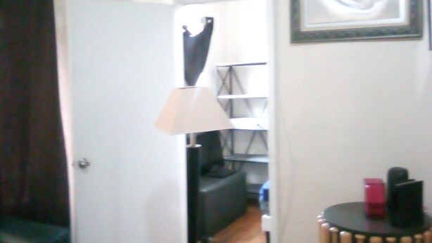 Une pièce avec une porte, une lampe, un tableau encadré au mur et une petite table ronde sur laquelle se trouvent divers objets.