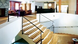 Vestíbulo de hotel con escalera, zona de estar y mostrador de recepción.