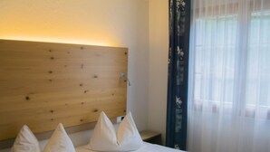 Una habitación de hotel con cabecera de madera, cama con ropa blanca y cortinas traslúcidas en la ventana.