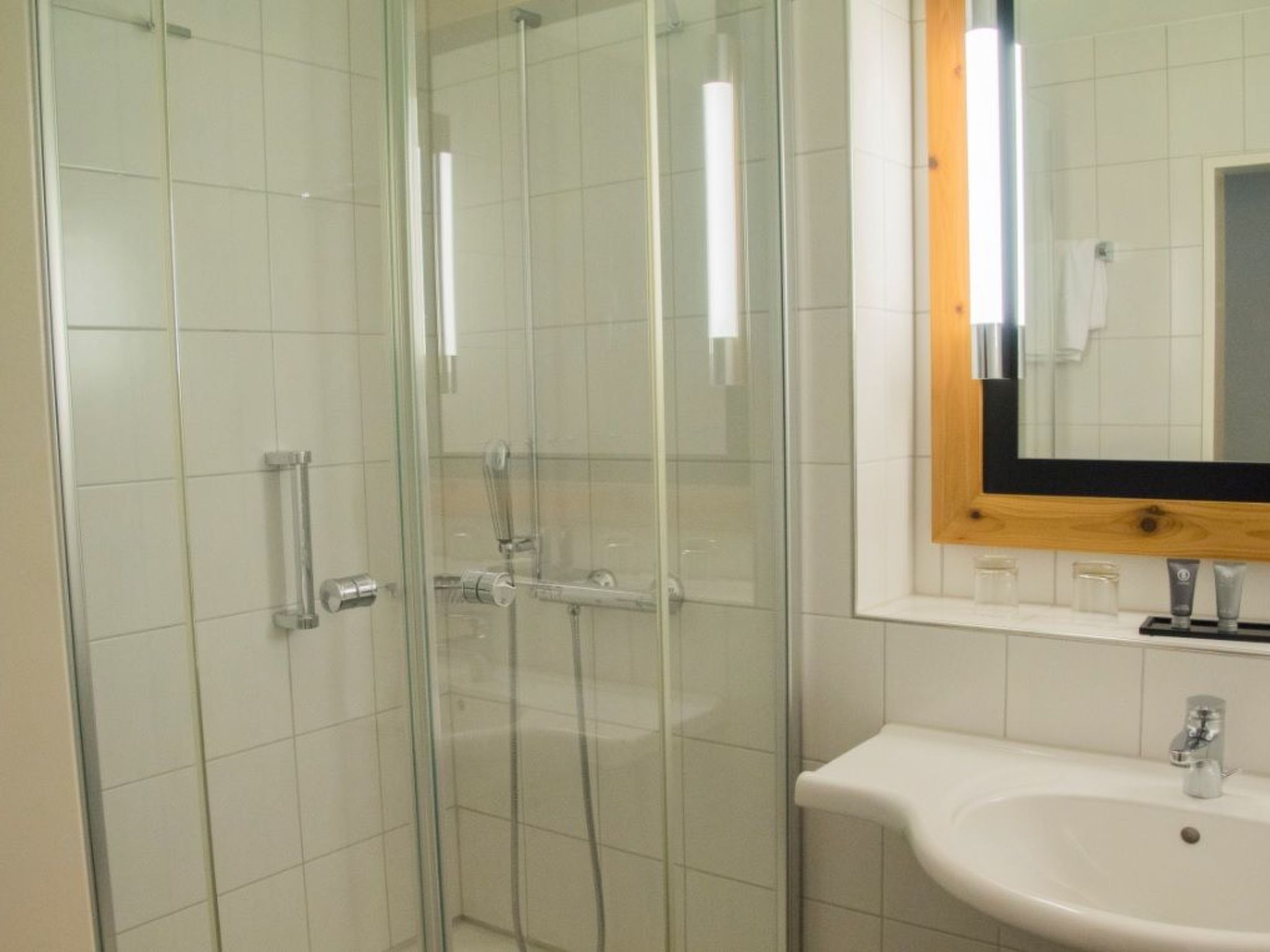 Une salle de bain avec une douche à parois de verre, un lavabo blanc et un miroir avec un cadre en bois.