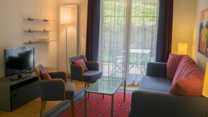 Una sala de estar con televisor, dos sillones, un sofá, una mesa de centro de vidrio y un tapete estampado.
