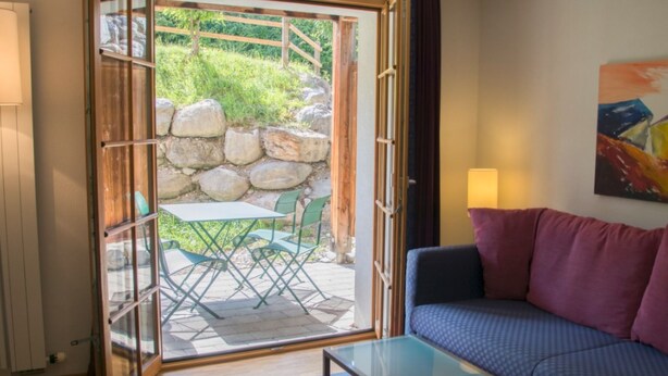 Una puerta corredera abierta que da a un patio con una mesa, sillas, un sofá y un cuadro en la pared.