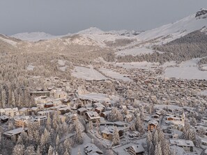 Une ville de montagne enneigée, avec des bâtiments regroupés autour d’un centre-ville, le tout entouré de pentes boisées et de montagnes.