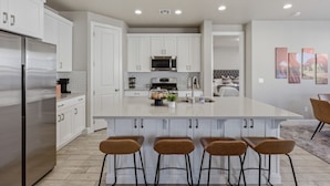 A modern kitchen with white cabinets, a stainless steel refrigerator, and a central island with bar stools.