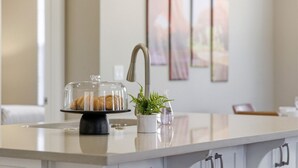 A kitchen counter with a glass dome cake stand, a potted plant, and a sink.