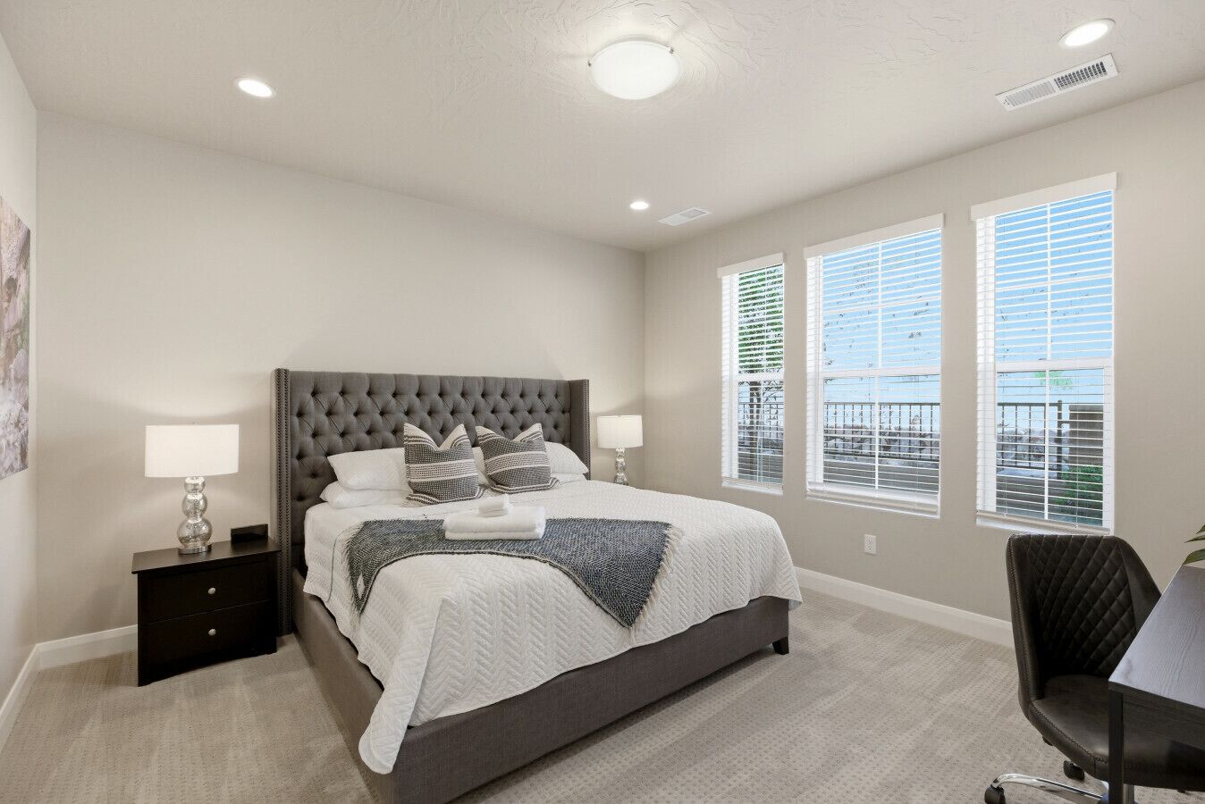 Une chambre à coucher avec un grand lit, deux tables de chevet, une chaise et une fenêtre avec des stores.