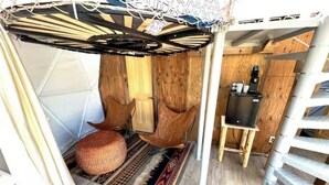 Huoneessa on puulattia, kuviollinen matto, pieni pyöreä rahi, tuoli ja TV-taso.