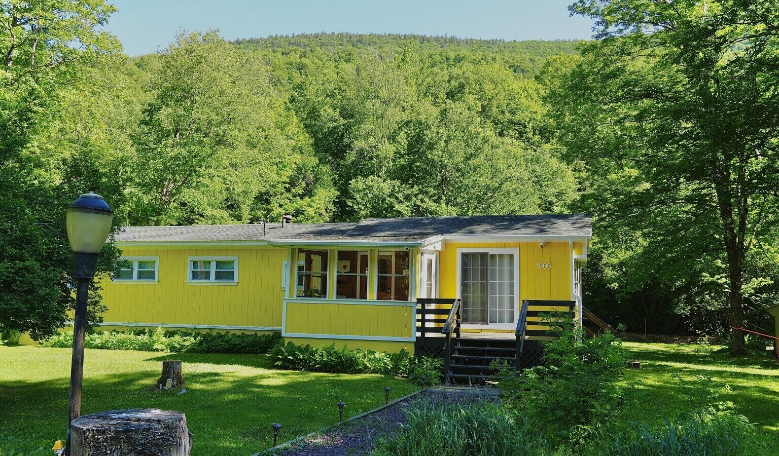 Eine gelbe Holzhütte mit Veranda und Treppe, umgeben von üppigem Grün.