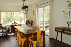 Un comedor con mesa de madera y sillas amarillas, ventanas amplias y vistas al exterior.