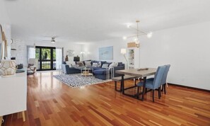 A spacious living area with a dining table, sofas, and a large window.