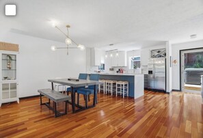 A modern kitchen with a central island, wooden flooring, and pendant lighting.