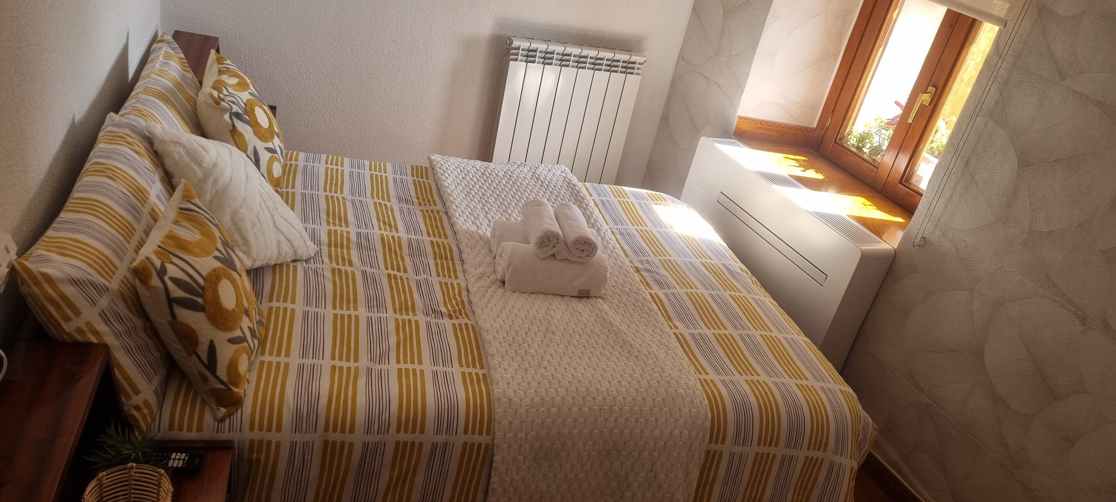 Un lit avec une literie à motifs, une table de chevet avec une télécommande et une fenêtre donnant sur un beau paysage.
