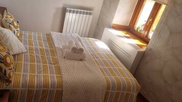 Una cama con ropa de cama estampada, una mesita de noche con un control remoto y una ventana con vistas.