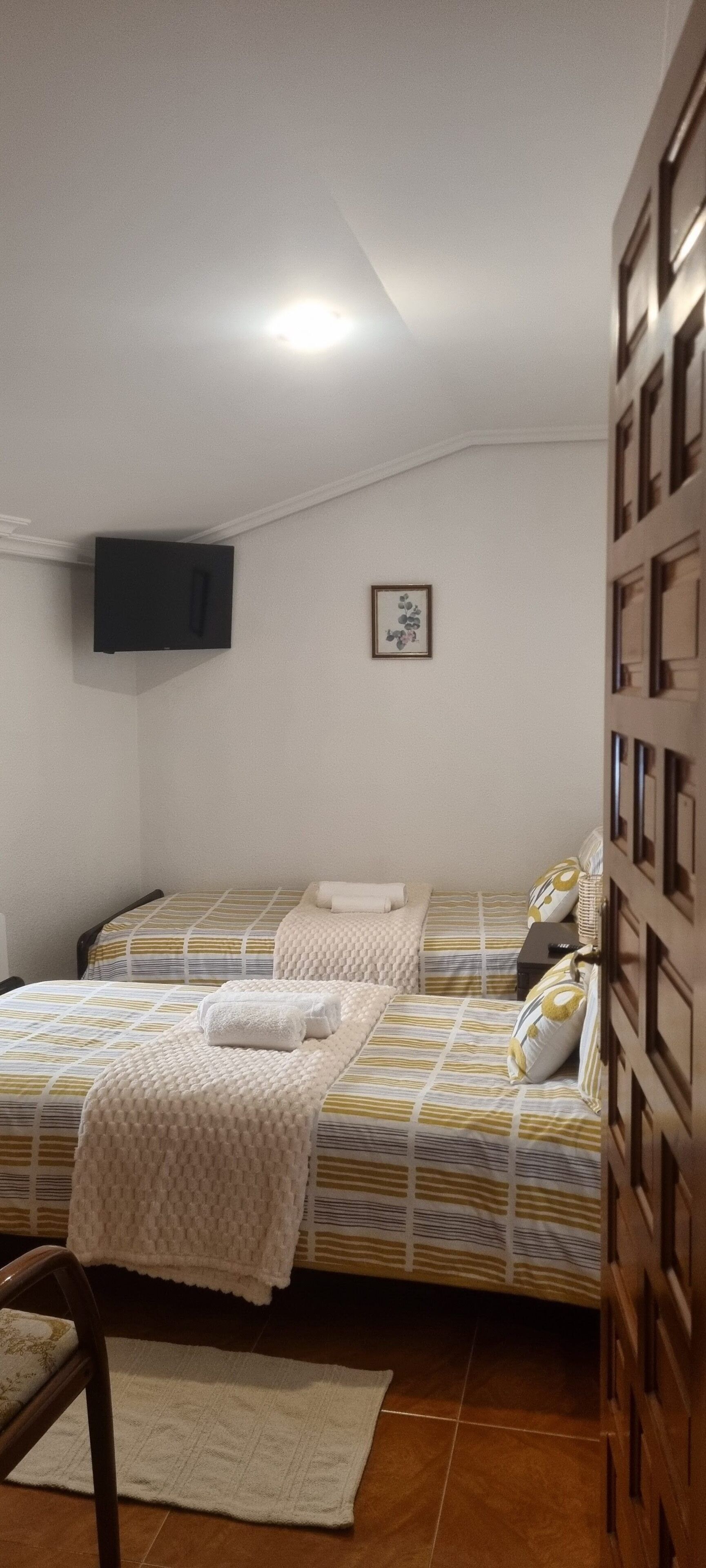 Slaapkamer met twee bedden, een flatscreen televisie aan de muur, een lijst met een afbeelding en een houten garderobe.