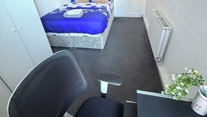 Ein kleiner, kompakter Raum mit Bett, Schreibtisch, Stuhl, Heizkörper und einer Tür.