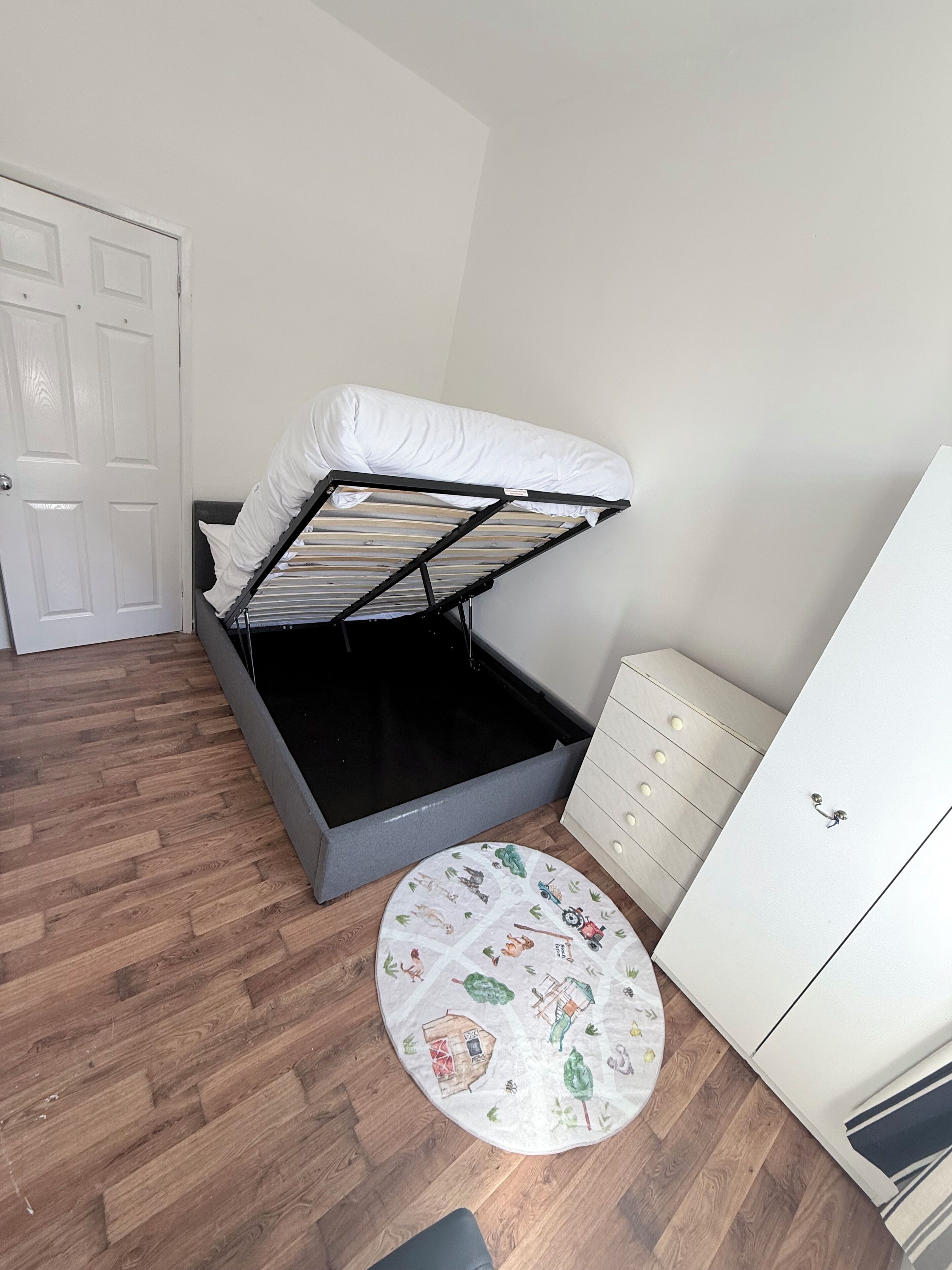 Een slaapkamer met een bed, een kaptafel, een rond tapijt en een deur.